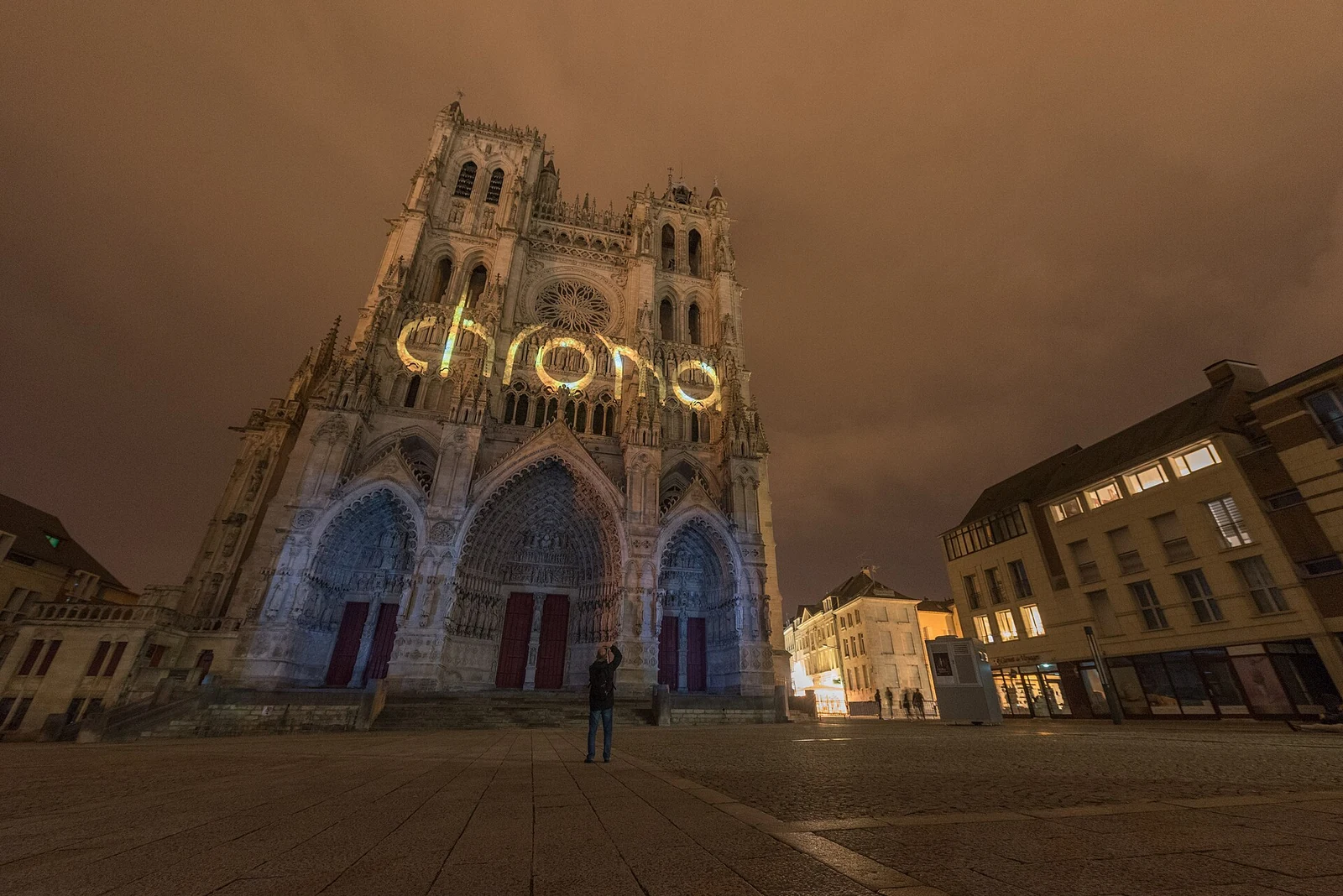 Projection lumineuse Chroma sur la façade de la cathédrale Notre-Dame d’Amiens, de nuit, avec un spectateur sur le parvis