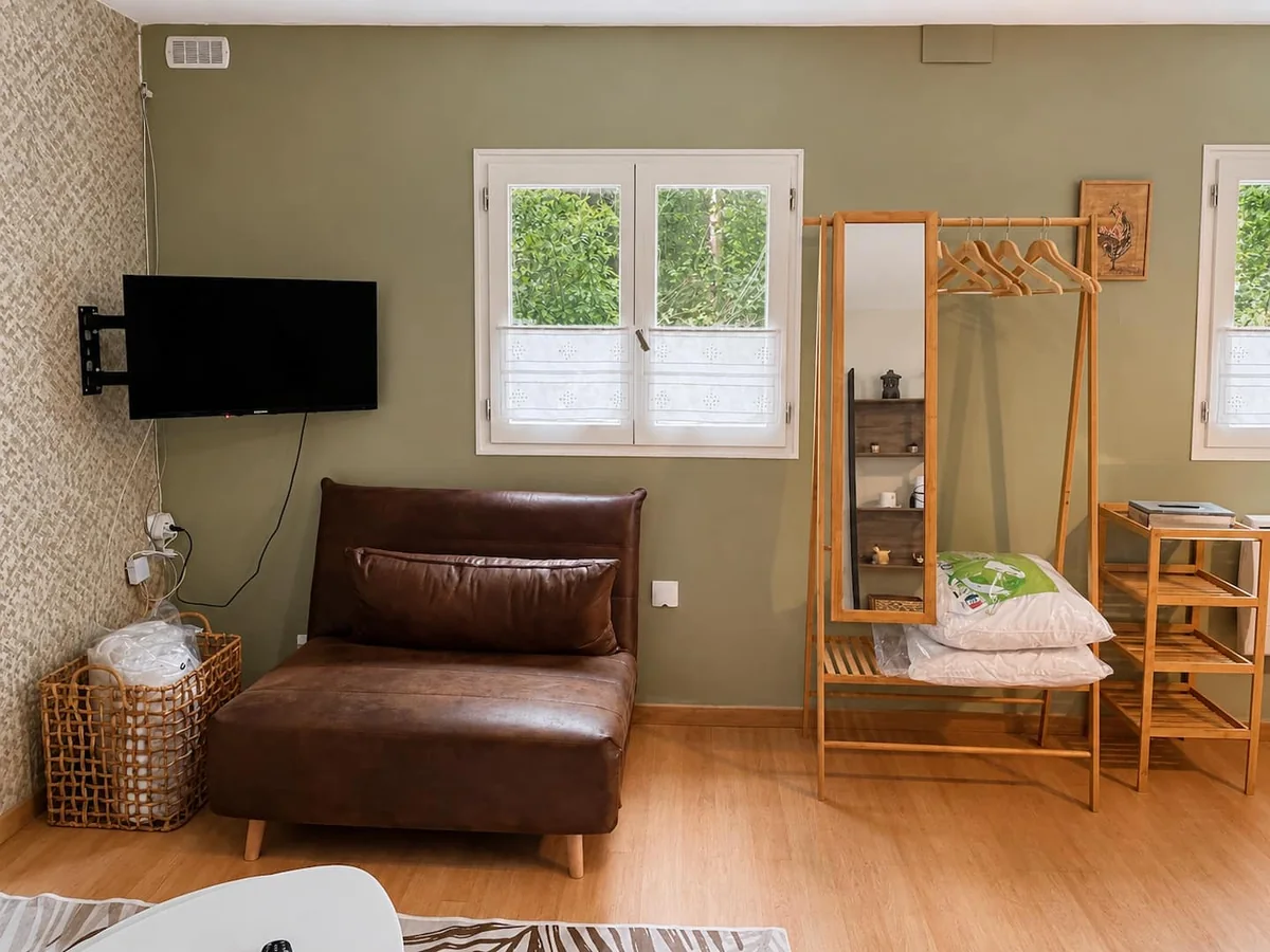 Le salon du logement avec canapé, télévision et fenêtres ouvertes sur la verdure