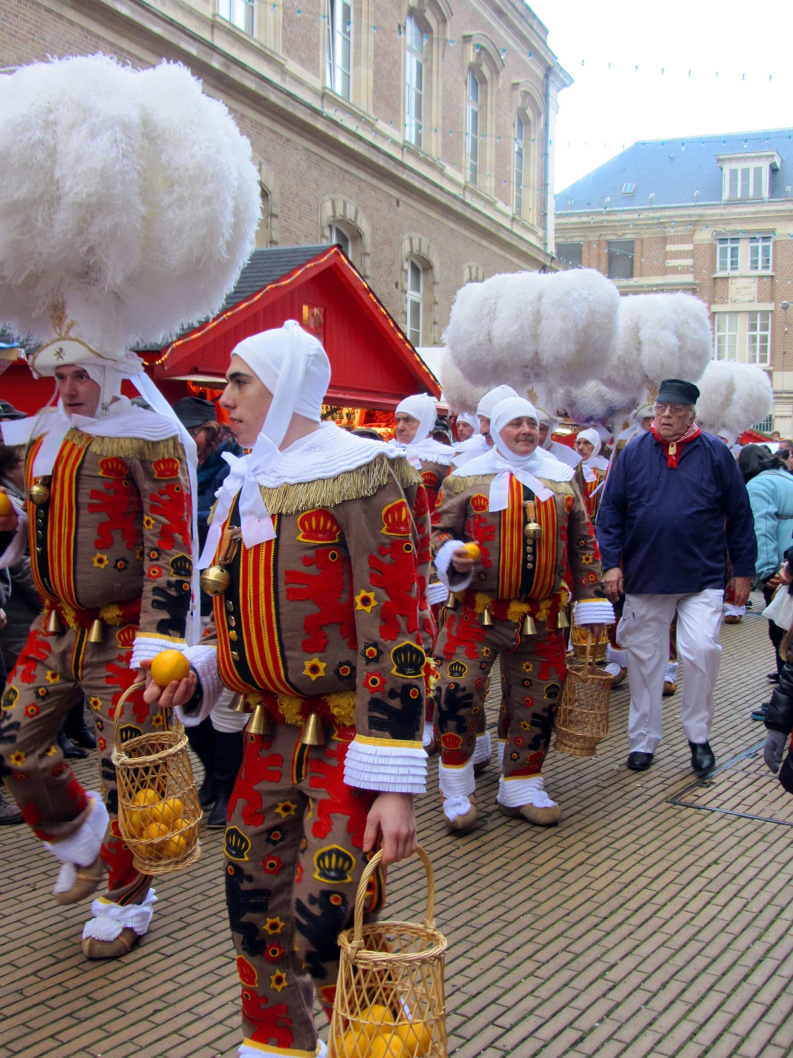 Défilé de Gilles de Binche en costume devant les chalets rouges du marché de Noël d’Amiens en 2013